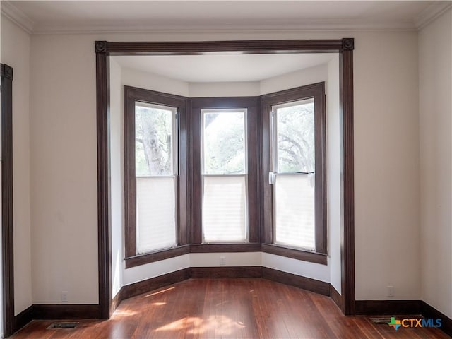 interior space with wood finished floors, visible vents, baseboards, and ornamental molding
