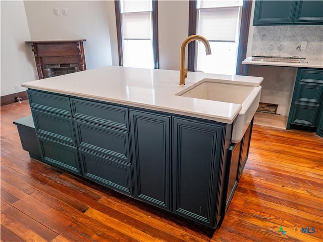 kitchen featuring a kitchen island with sink, a sink, dark wood finished floors, decorative backsplash, and light countertops