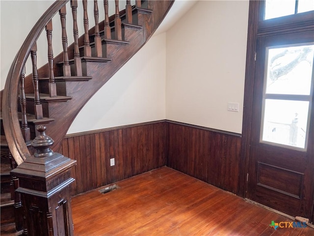 foyer featuring wooden walls, wood finished floors, visible vents, and a wainscoted wall