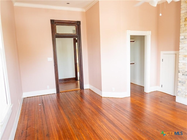 empty room with wood-type flooring, a ceiling fan, baseboards, and ornamental molding