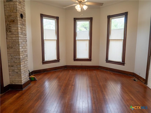 empty room featuring crown molding, ceiling fan, baseboards, dark wood-type flooring, and visible vents