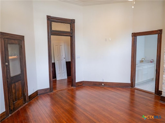 empty room with wood-type flooring, baseboards, crown molding, and a sink