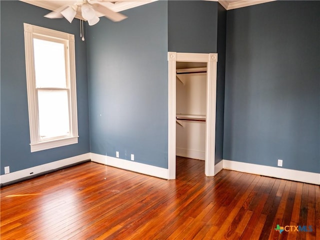 unfurnished bedroom with hardwood / wood-style flooring, baseboards, crown molding, and a closet