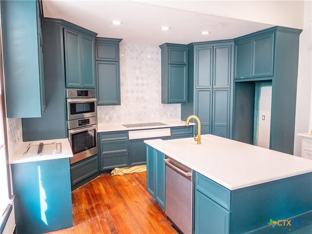 kitchen featuring light wood finished floors, stainless steel appliances, light countertops, a sink, and blue cabinetry