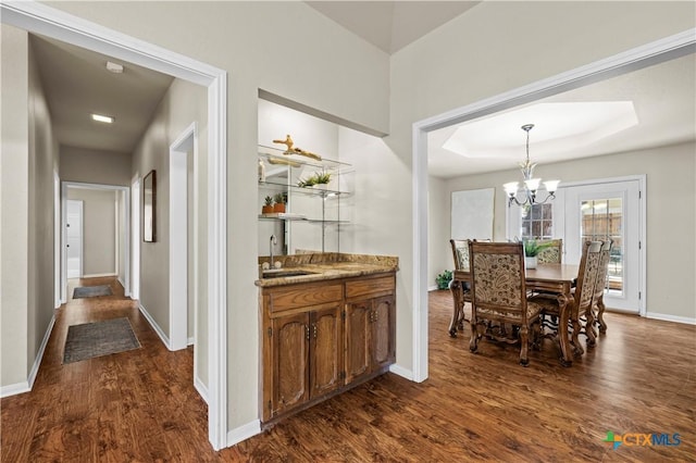 dining area featuring sink, a notable chandelier, dark hardwood / wood-style floors, and a tray ceiling