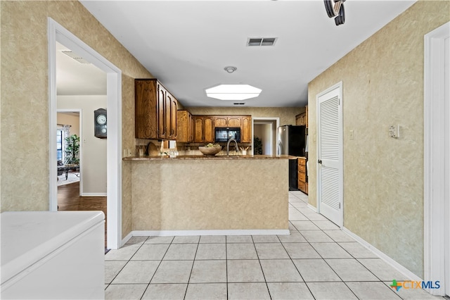 kitchen with sink, kitchen peninsula, light tile patterned flooring, and stainless steel fridge