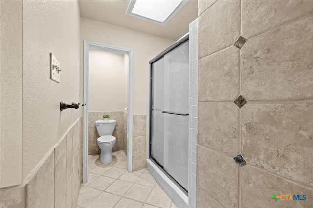 bathroom with toilet, tile patterned floors, an enclosed shower, and tile walls