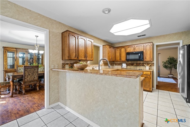 kitchen featuring kitchen peninsula, light tile patterned floors, decorative backsplash, stainless steel refrigerator, and sink