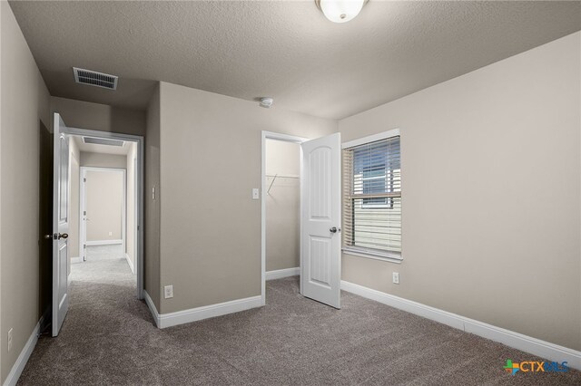 unfurnished bedroom with carpet, a textured ceiling, a walk in closet, and a closet