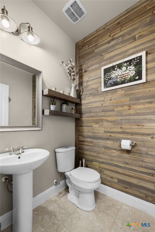 bathroom with wood walls, tile patterned flooring, sink, and toilet