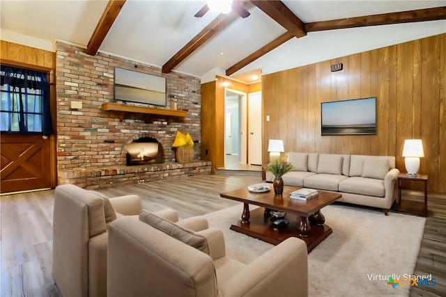 living room with wood walls, ceiling fan, light hardwood / wood-style flooring, a brick fireplace, and lofted ceiling with beams