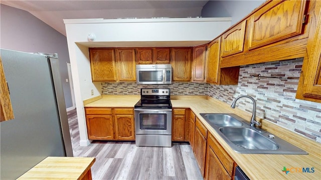 kitchen with appliances with stainless steel finishes, lofted ceiling, light hardwood / wood-style floors, sink, and backsplash