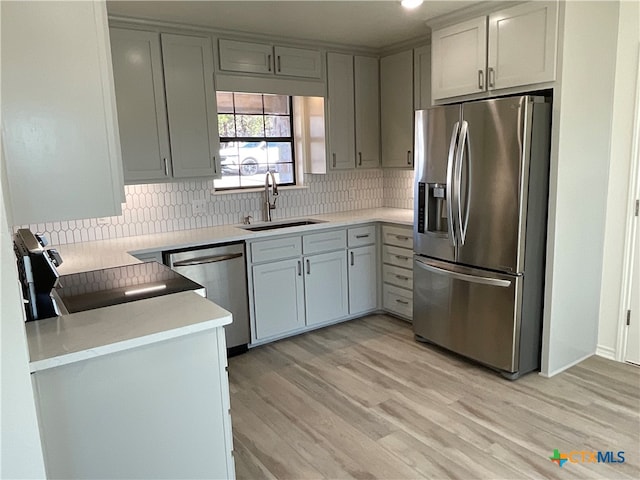 kitchen featuring gray cabinetry, stainless steel appliances, decorative backsplash, sink, and light hardwood / wood-style floors