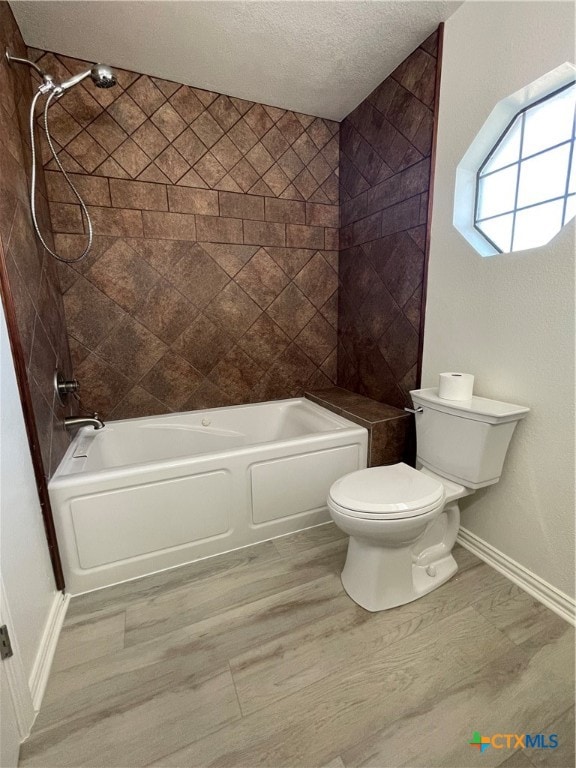 bathroom with tiled shower / bath combo, hardwood / wood-style floors, a textured ceiling, and toilet