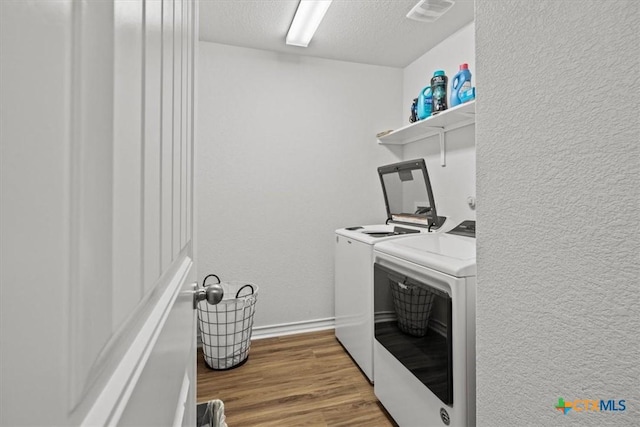 clothes washing area featuring hardwood / wood-style floors, washer and dryer, and a textured ceiling