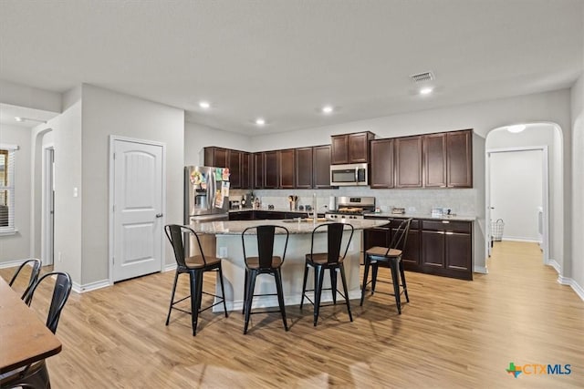 kitchen with dark brown cabinetry, a kitchen bar, tasteful backsplash, appliances with stainless steel finishes, and an island with sink