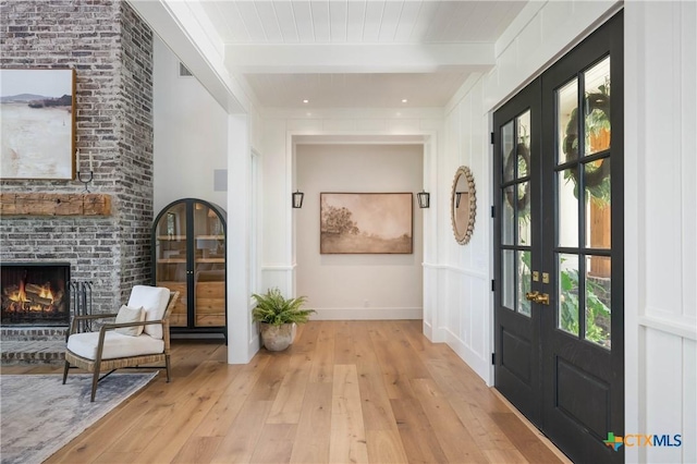 foyer entrance featuring beam ceiling, hardwood / wood-style floors, french doors, baseboards, and a brick fireplace