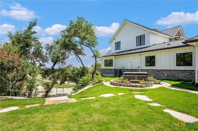 back of house with central AC unit, a standing seam roof, a lawn, brick siding, and metal roof