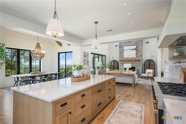 kitchen with visible vents, a brick fireplace, light brown cabinetry, light wood-style flooring, and exhaust hood