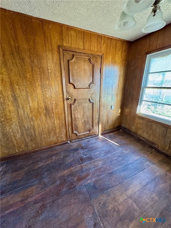 unfurnished room with wooden walls, dark wood-type flooring, and a textured ceiling