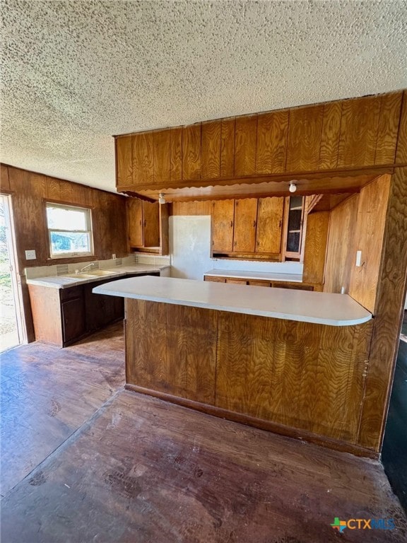 kitchen featuring kitchen peninsula, dark hardwood / wood-style flooring, a textured ceiling, sink, and wood walls