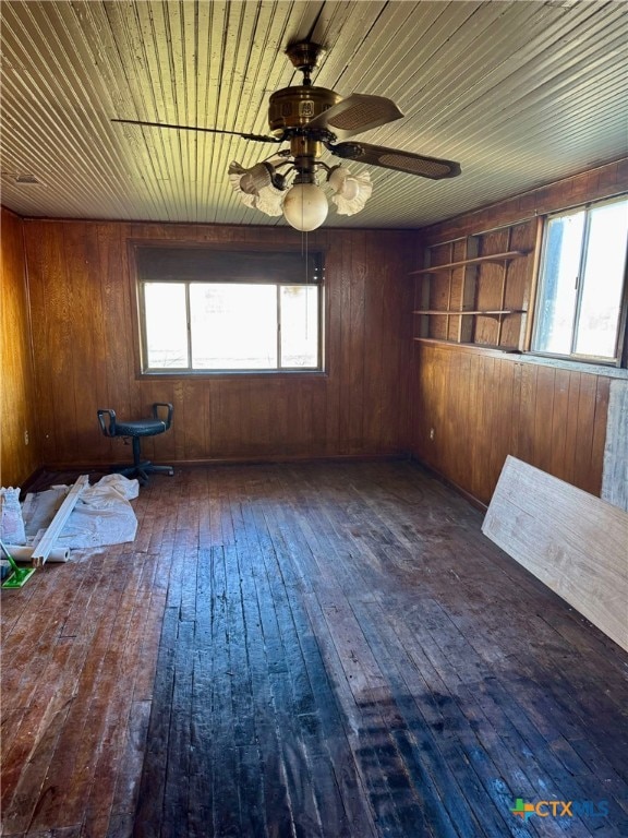 unfurnished room featuring wood walls, ceiling fan, a healthy amount of sunlight, and dark hardwood / wood-style flooring