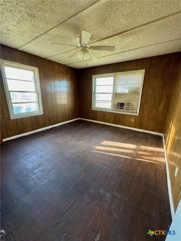 empty room featuring wooden walls, plenty of natural light, and dark wood-type flooring