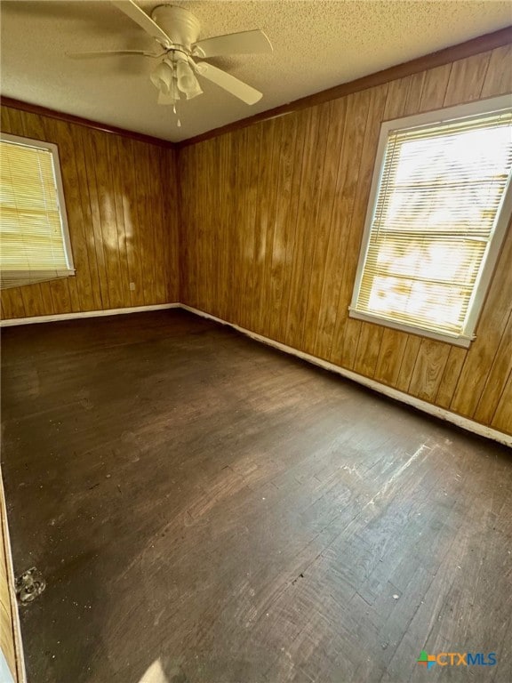 empty room with a textured ceiling, ceiling fan, dark wood-type flooring, and wood walls