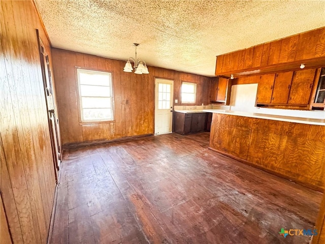 kitchen with hanging light fixtures, dark wood-type flooring, a notable chandelier, kitchen peninsula, and wooden walls