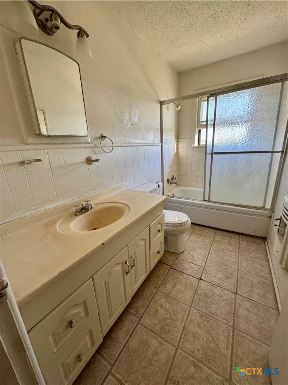 full bathroom with vanity, tile patterned floors, bath / shower combo with glass door, toilet, and a textured ceiling