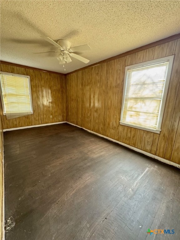 unfurnished room featuring a textured ceiling, wooden walls, ceiling fan, and dark wood-type flooring