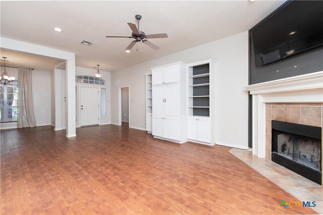 unfurnished living room featuring a fireplace, ceiling fan with notable chandelier, wood finished floors, and visible vents