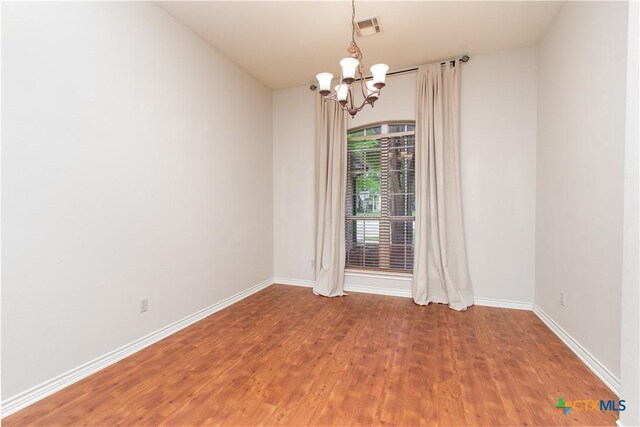 empty room with baseboards, visible vents, light wood finished floors, and a chandelier