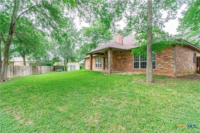 view of yard featuring an outbuilding, a patio area, fence, and a storage shed