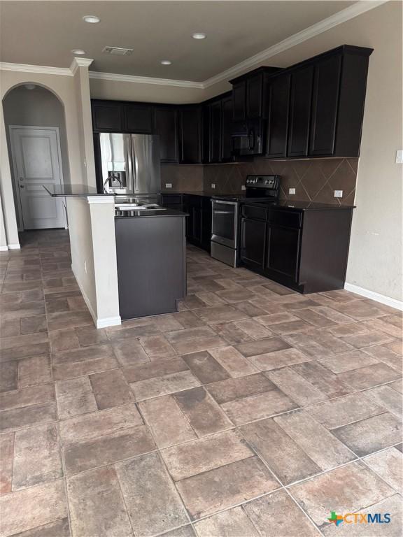 kitchen with arched walkways, dark cabinets, stainless steel appliances, and tasteful backsplash