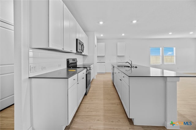 kitchen featuring appliances with stainless steel finishes, sink, light wood-type flooring, white cabinetry, and an island with sink