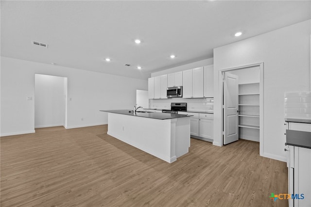 kitchen featuring light wood-type flooring, white cabinets, a kitchen island with sink, and stainless steel appliances