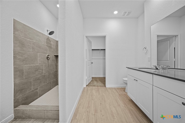 bathroom featuring toilet, tiled shower, wood-type flooring, and vanity