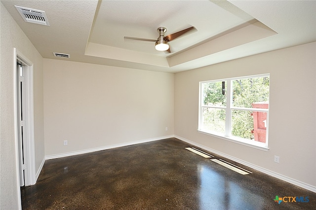 empty room featuring a tray ceiling, ceiling fan, and a textured ceiling