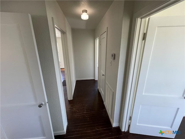 corridor with dark wood-type flooring and a textured wall