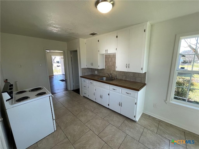 kitchen featuring plenty of natural light, white range with electric stovetop, visible vents, a sink, and backsplash