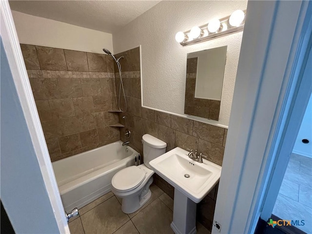 bathroom with toilet, shower / tub combination, tile patterned flooring, a textured ceiling, and tile walls