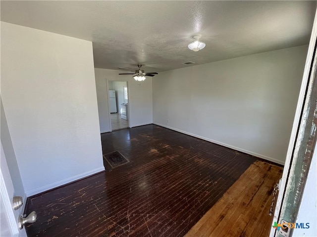 empty room with visible vents, dark wood finished floors, baseboards, and ceiling fan