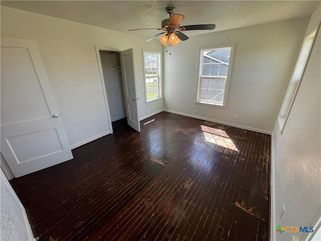 unfurnished bedroom with dark wood-style floors, a closet, a ceiling fan, and baseboards