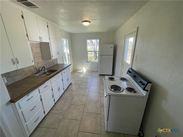 kitchen featuring a textured ceiling, white appliances, a sink, white cabinetry, and decorative backsplash