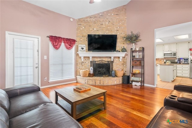 living area featuring baseboards, lofted ceiling, light wood-style floors, and a brick fireplace