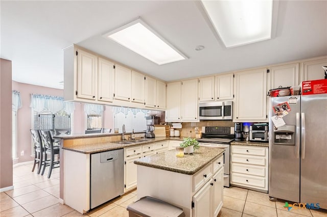 kitchen featuring light stone countertops, appliances with stainless steel finishes, a peninsula, light tile patterned flooring, and a sink