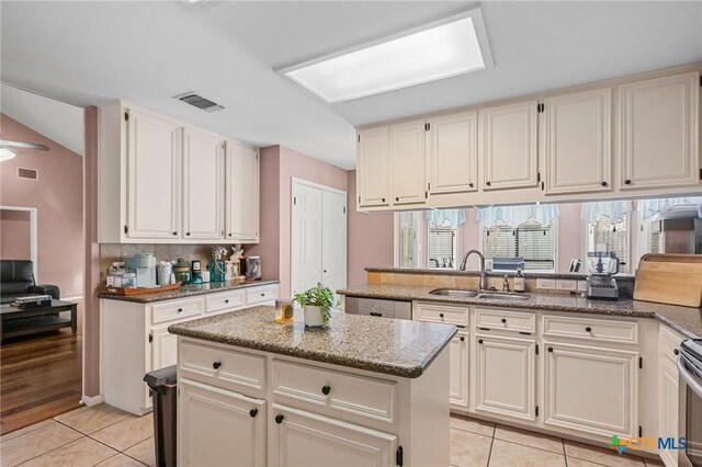 kitchen with visible vents, a sink, stone countertops, a center island, and light tile patterned floors