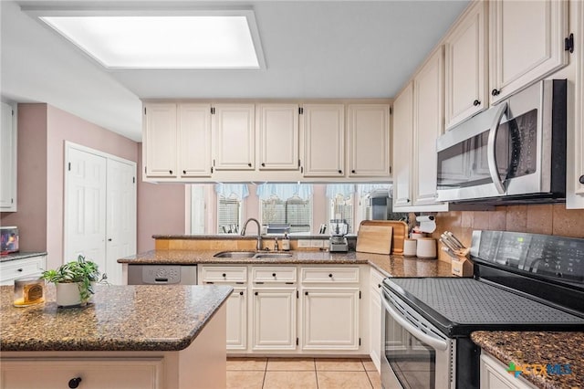 kitchen featuring dark stone counters, a peninsula, light tile patterned flooring, a sink, and stainless steel appliances