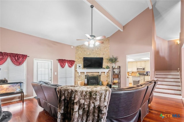 living room featuring beam ceiling, a brick fireplace, a ceiling fan, and wood finished floors